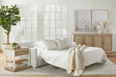 a white bed sitting on top of a wooden floor next to a table with a potted plant