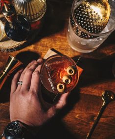 a person holding a drink with olives in it on a table next to other items