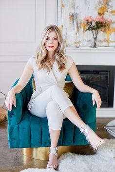 a woman sitting on top of a blue chair in front of a fireplace with her legs crossed