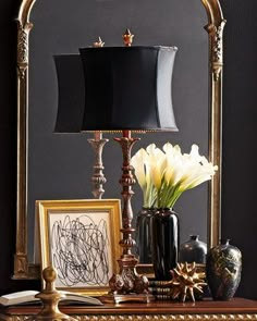 a table with a lamp, vases and pictures on top of it in front of a mirror