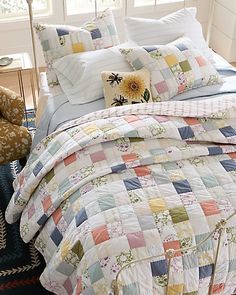 a bed with colorful quilts and pillows in a room next to a chair on the floor