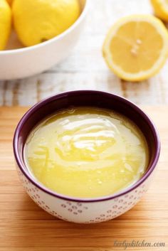 a bowl filled with yellow liquid next to some lemons on a wooden cutting board