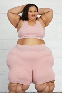 a woman posing for the camera in her pink shorts and sports bra, with one hand on her head