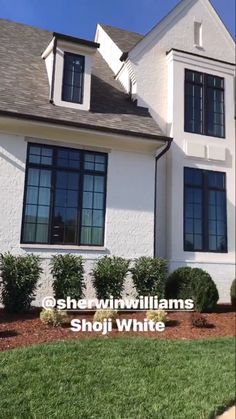 a white house with black windows and bushes