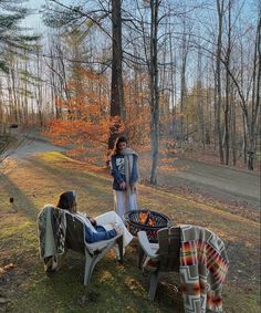 two women standing next to each other near a fire pit in the middle of a forest