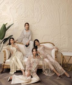 four women sitting on a white couch in front of a wallpapered room with plants