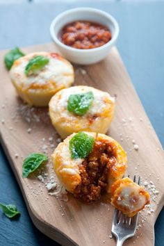 three mini pizzas on a wooden cutting board with a fork next to them and basil leaves