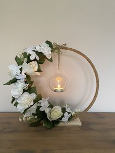 a wreath with white flowers and a lit candle in the center on a wooden table