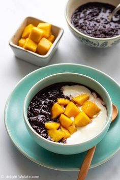 a bowl of fruit and yogurt on a plate with spoons next to it