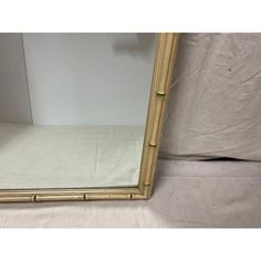 a gold bamboo framed mirror sitting on top of a white sheeted bedding area