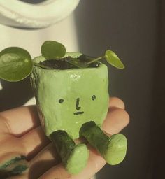 a hand holding a small green plant in it's left side, with a face drawn on the top