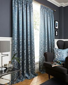 a living room with blue curtains and a chair in front of a window that has an ornate pattern on it