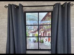 an open window with black curtains in front of a white brick wall and mountain view