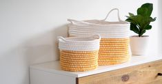 two baskets sitting on top of a dresser next to a potted plant