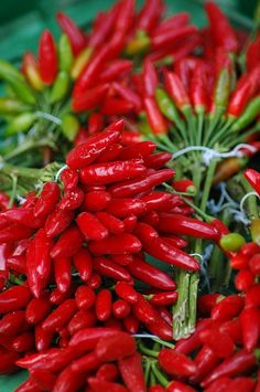 red peppers are piled on top of each other with green stems in the foreground