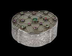 an ornate silver box with various colored stones on the lid and sides, sitting in front of a black background