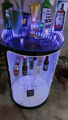 an illuminated bar cart with liquor bottles and glasses on the top, in front of a potted plant