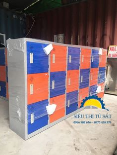 several stacks of orange, blue and grey boxes in a storage area with shipping containers behind them