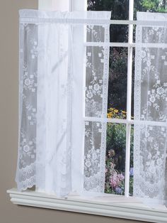 an open window with white lace curtains and flowers in the window sill next to it