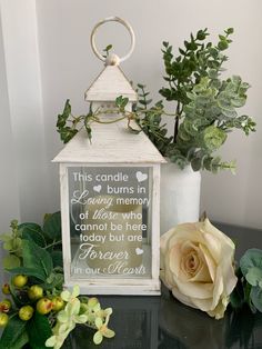 a small white lantern sitting on top of a table next to flowers and greenery