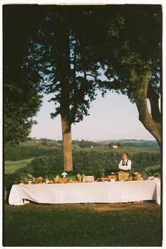 a man sitting at a table with food on it in the middle of a field