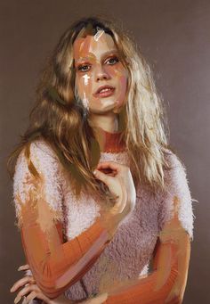 a woman is posing with her hands on her chest and face painted in orange, white and pink