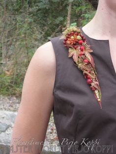 a woman wearing a brown dress with red flowers on it's neck and in front of some trees