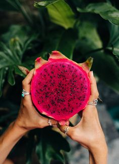 two hands holding up a piece of fruit in front of some green plants and leaves