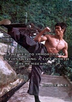 a shirtless man doing a kickbox pose in front of some rocks and trees