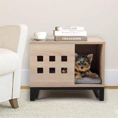 a small dog sitting in a wooden crate on the floor next to a white chair