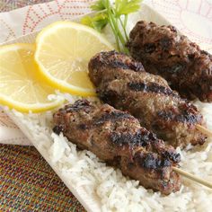 two skewers of meat and rice on a plate with lemon wedges, garnished with parsley