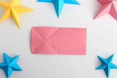 four origami stars and one pink rectangle on a white background with an empty piece of paper