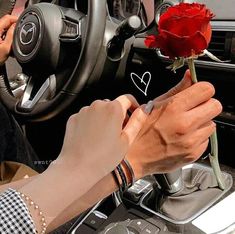 a person holding a red rose in their hand while sitting in the driver's seat of a car