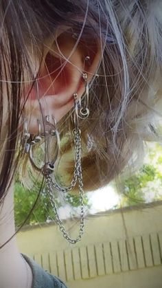 a woman with long hair wearing silver ear rings and chains on her ears is looking out the window