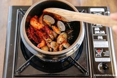 clams being cooked in a pot on top of an electric stove with a wooden spoon