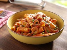 a yellow bowl filled with pasta and meat on top of a wooden table next to a fork