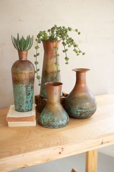 three vases sitting on top of a wooden table next to a potted plant