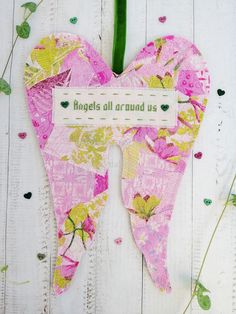 a pink heart shaped piece with words on it and flowers in the middle, sitting on a white wooden surface