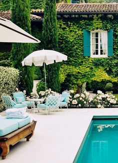 an outdoor pool with chairs and umbrellas next to a building covered in ivy, surrounded by white flowers