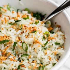 a white bowl filled with rice and topped with chopped green onions, carrots and seasoning