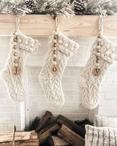 christmas stockings hanging from a mantel in front of a fireplace with logs and pine cones