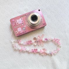 a pink digital camera sitting on top of a white tablecloth next to a lanyard