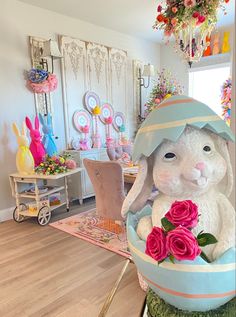 an easter bunny sitting in a basket with flowers on the table and other decorations behind it