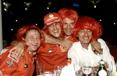 three men in red wigs are hugging each other at a table with drinks and wine glasses