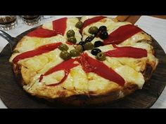 a pizza with olives and cheese on a wooden platter next to wine glasses