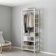 a white closet with clothes hanging on the wall and a chair in front of it