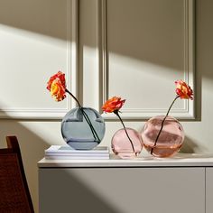 three vases with flowers in them sitting on a table next to a chair and wall