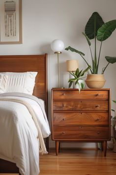 a bedroom with a bed, dresser and potted plant on the nightstand next to it