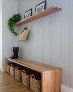 a wooden bench with baskets underneath it and two framed pictures on the wall behind it