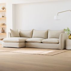 a living room with white walls and wooden flooring is pictured in this image, there is a large sectional couch on the far side